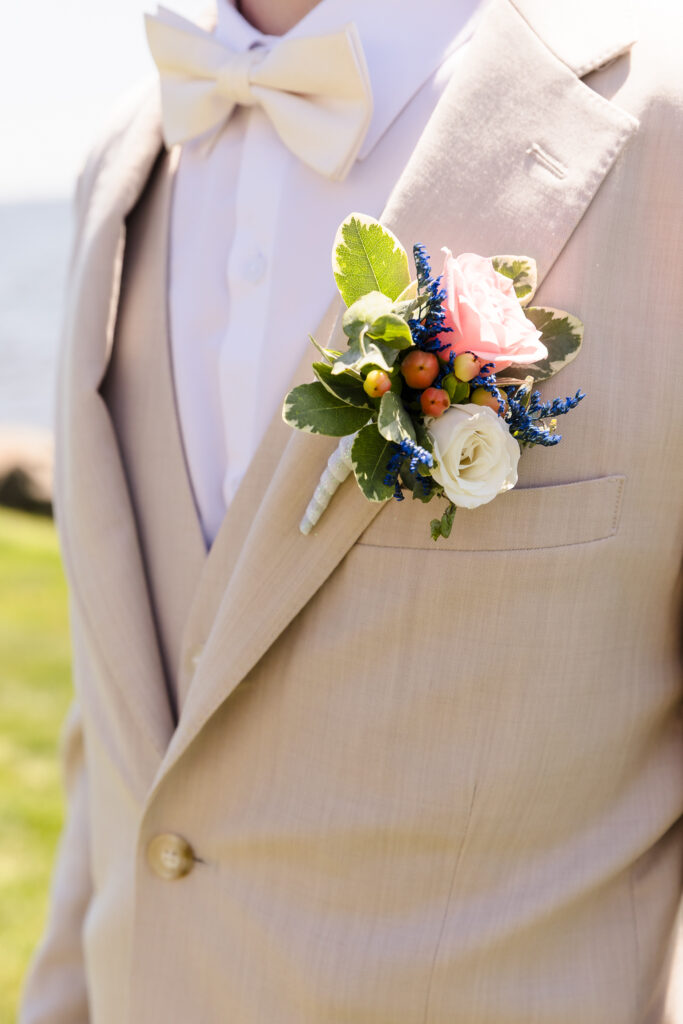 Close-up of groom’s tan suit with ivory bow tie and pink and white rose boutonniere at Camp Pa-Qua-Tuck wedding on Long Island.