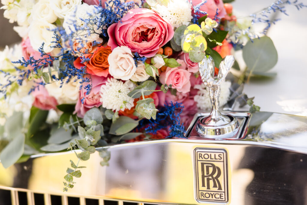 Bridal bouquet of pink, orange, and white flowers resting on the hood of a Rolls Royce at Sabrina and Matt’s Camp Pa-Qua-Tuck wedding.