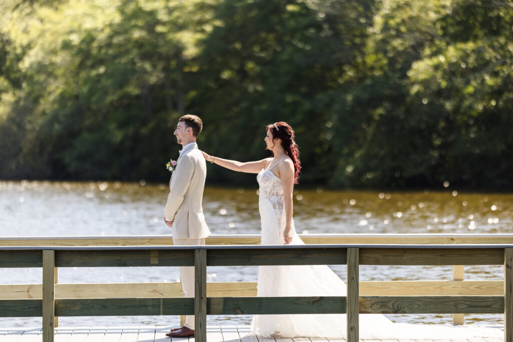 Bride tapping groom on the shoulder during their emotional first look on the dock at Camp Pa-Qua-Tuck in Long Island.