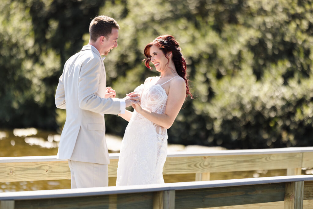 Bride and groom laughing and holding hands during their first look on the dock at Camp Pa-Qua-Tuck in Long Island.