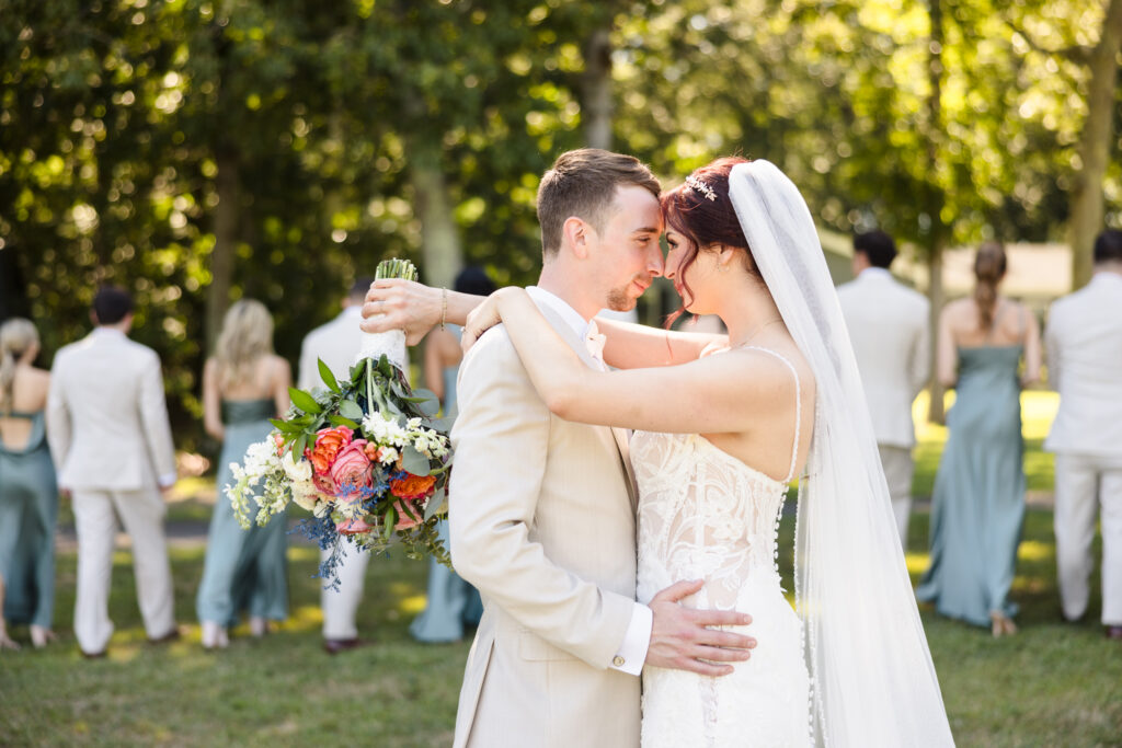 Bride and groom embracing with foreheads touching, holding a vibrant bouquet during their Camp Pa-Qua-Tuck wedding.