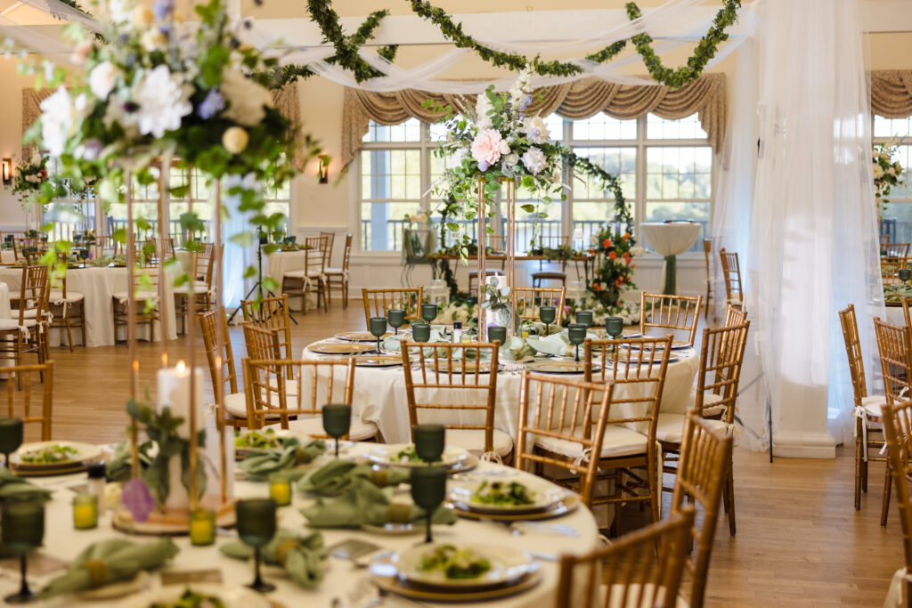 Camp Pa-Qua-Tuck wedding reception hall decorated with tall floral centerpieces, greenery garlands, and gold chiavari chairs.