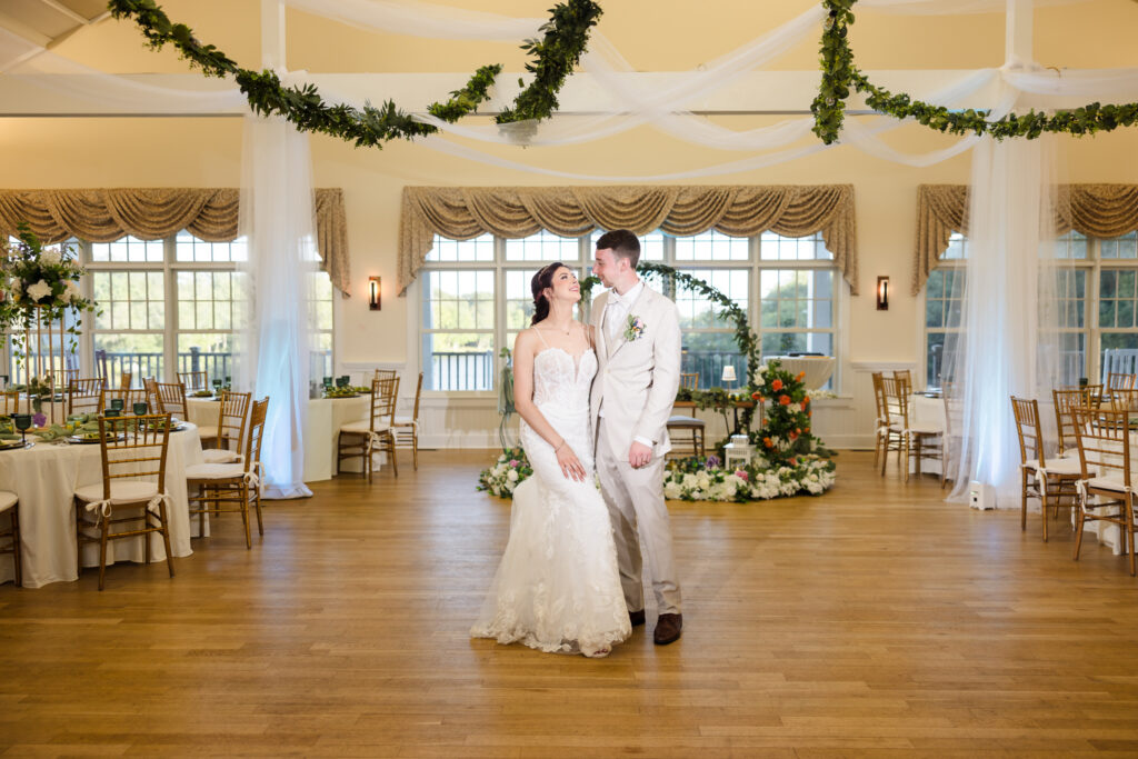 Bride and groom smiling at each other while standing in the decorated reception hall at Camp Pa-Qua-Tuck.