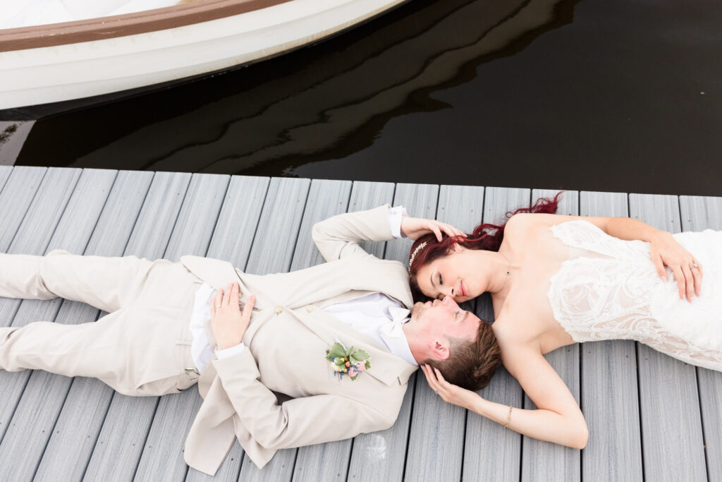 Bride and groom lying on the dock by the water, holding each other tenderly during their Camp Pa-Qua-Tuck wedding.