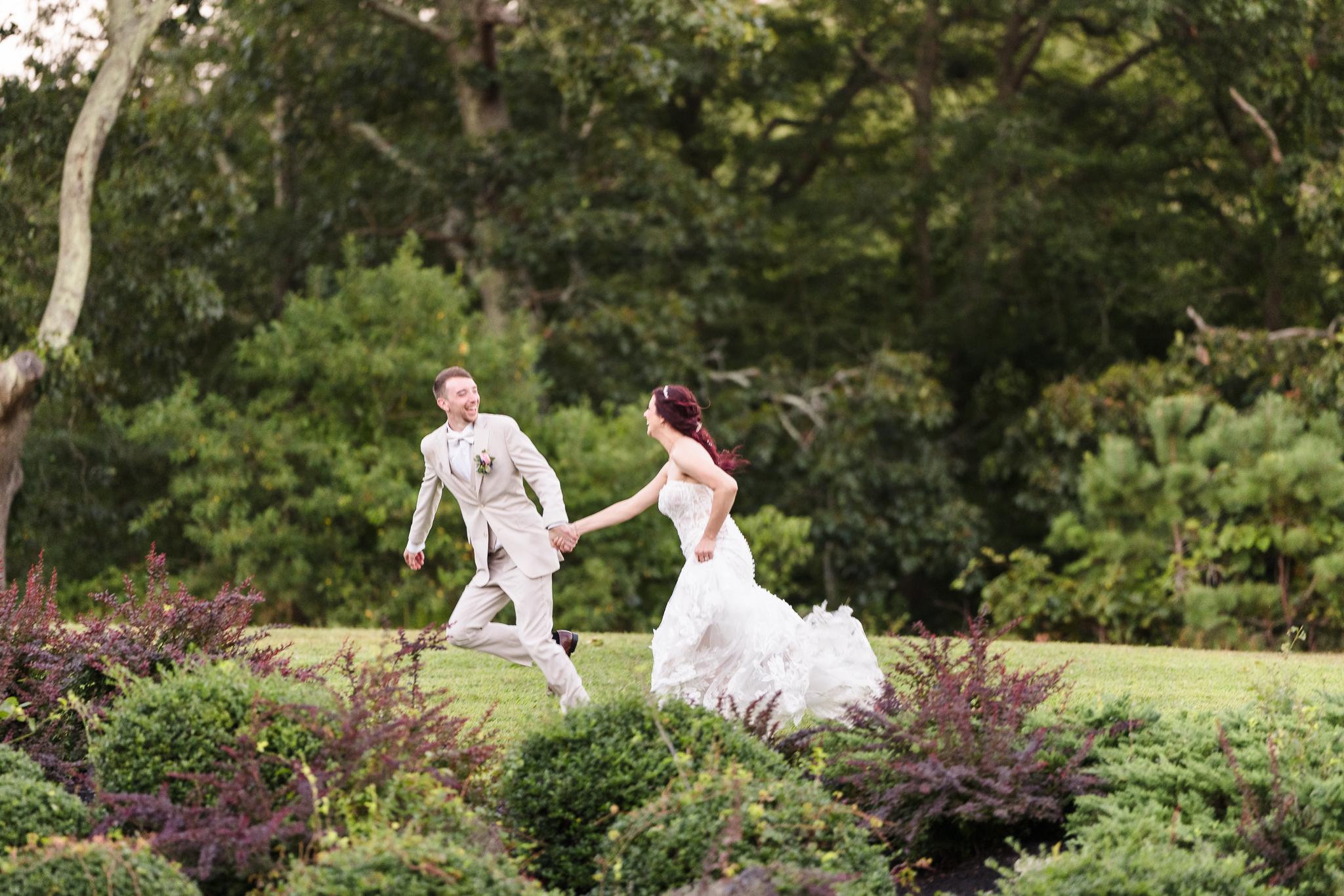 Bride Sabrina and groom Matt running hand in hand through the garden at Camp Pa-Qua-Tuck during their wedding day.
