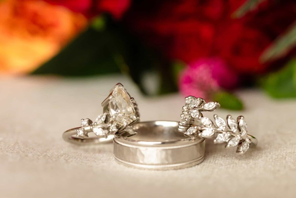 Close-up of diamond engagement ring, wedding band, and jeweled bridal ring with floral details at a luxury St. Regis New York wedding.