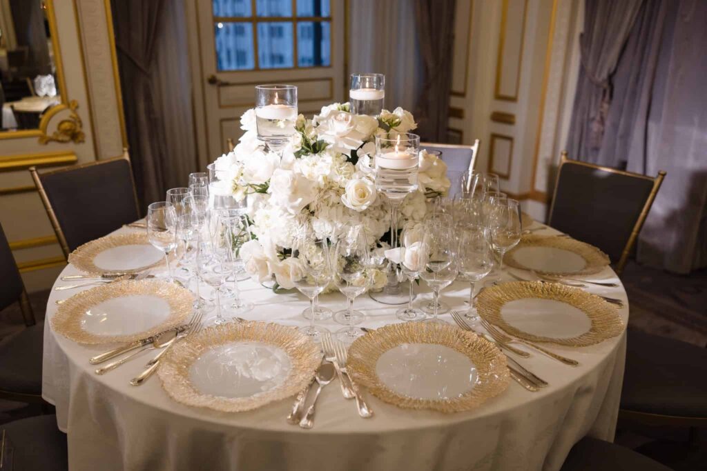 Wedding reception table at the St. Regis New York with gold-rimmed chargers, crystal glassware, white floral centerpiece, and floating candles.