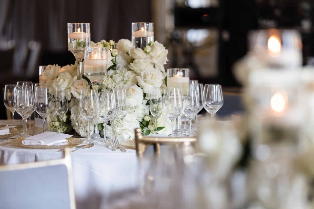 Romantic wedding table setting with white roses, hydrangeas, floating candles, and crystal glassware.