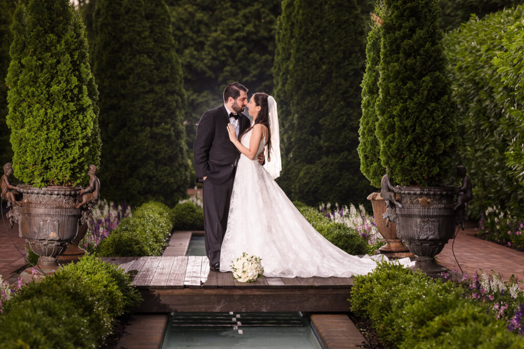 Bride and groom share a romantic moment in the lush gardens at Larkfield Manor, surrounded by greenery and classic European-style landscaping on Long Island.