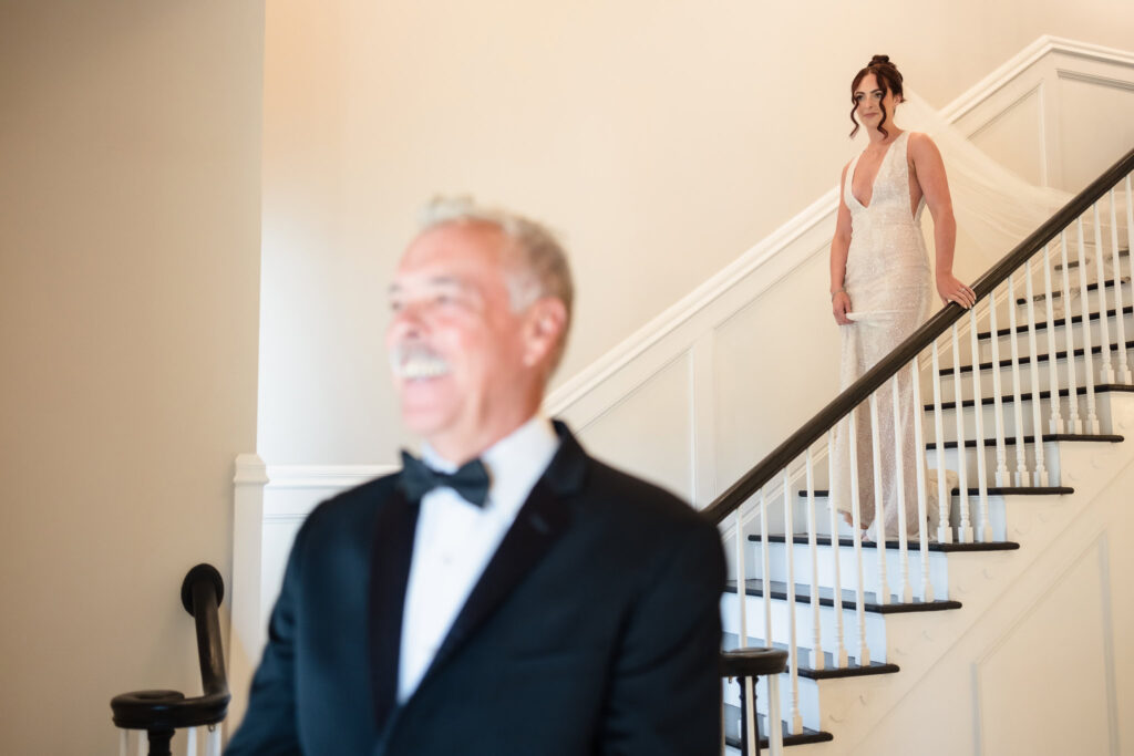 Bride in a beaded Tony Ward gown descends the staircase for an emotional first look with her father at Hiland Park Country Club, captured in soft natural light.