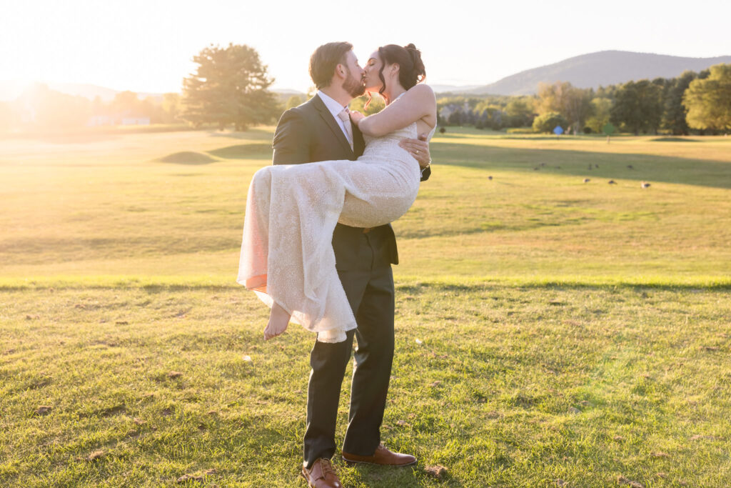 Groom lifts and kisses his bride in a joyful golden hour moment on the golf course at Hiland Park Country Club, surrounded by soft sunlight and mountain views.