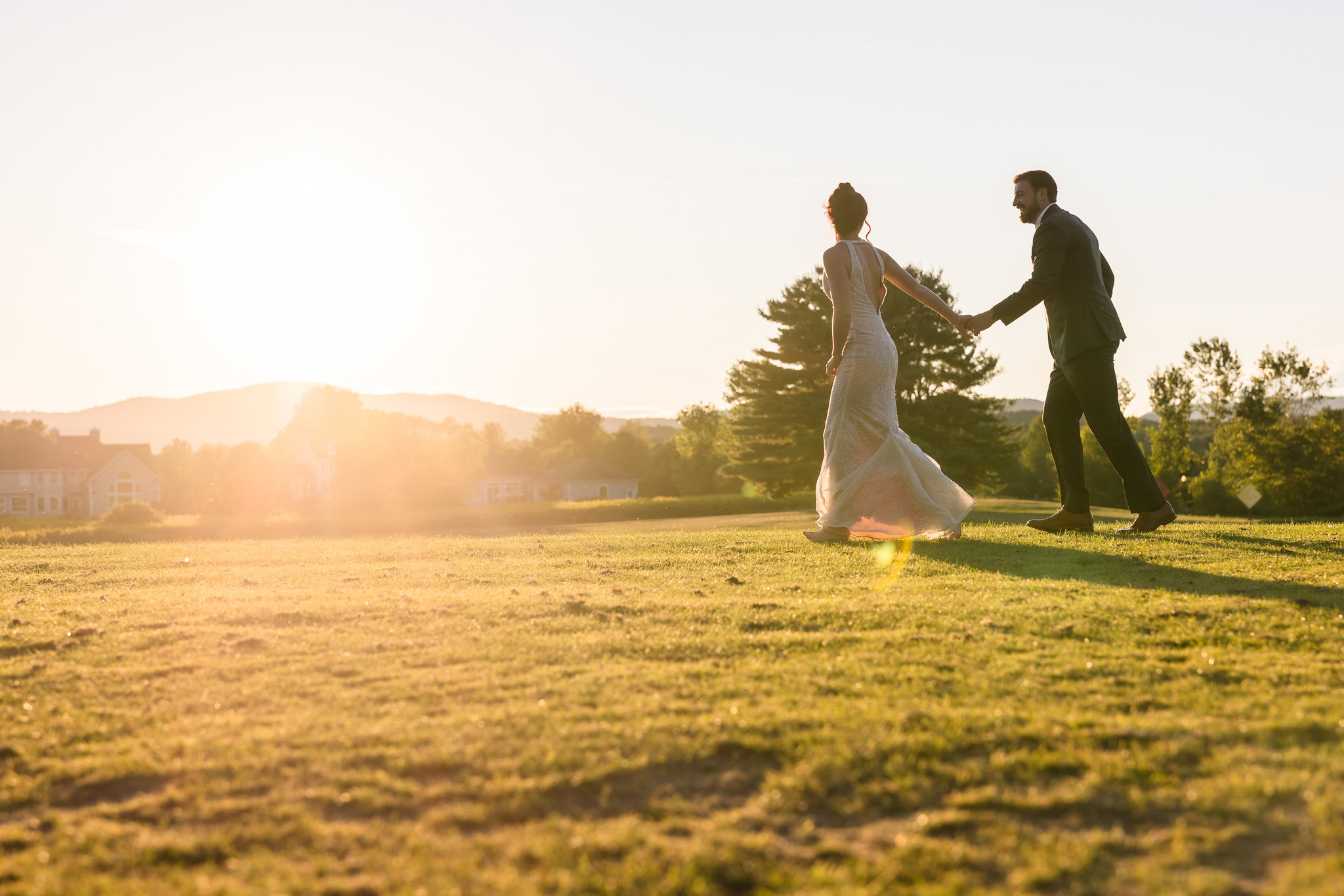 Bride leads groom across the sunlit hills of Hiland Park Country Club during golden hour, with soft sunset light casting romantic shadows on the golf course.