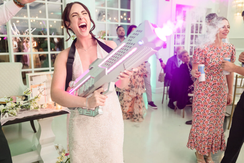 Bride laughing joyfully as she fires a CO2 cannon during the wedding reception at Hiland Park Country Club, bringing high-energy fun to the dance floor celebration.