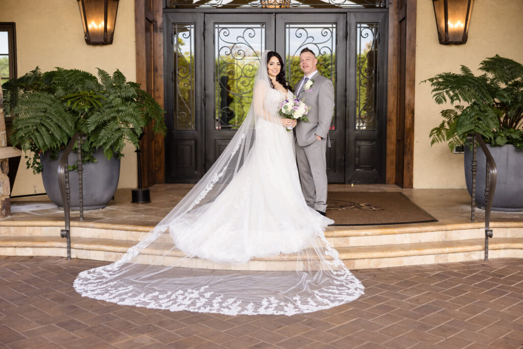 Bride and groom pose in front of Larkfield Manor’s grand entrance, with the bride’s cathedral-length lace veil flowing down the stone steps.