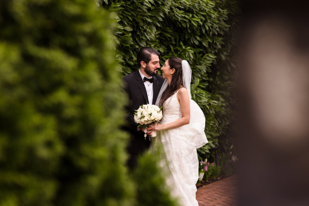 Bride and groom share an intimate moment in the lush garden walkway at Larkfield Manor, surrounded by greenery and classic Long Island elegance.