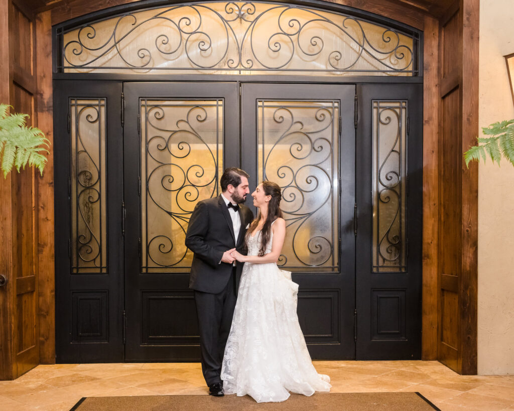 Bride and groom share a quiet moment in front of the grand wrought iron doors at Larkfield Manor, showcasing the venue’s elegant Tuscan-inspired entrance.