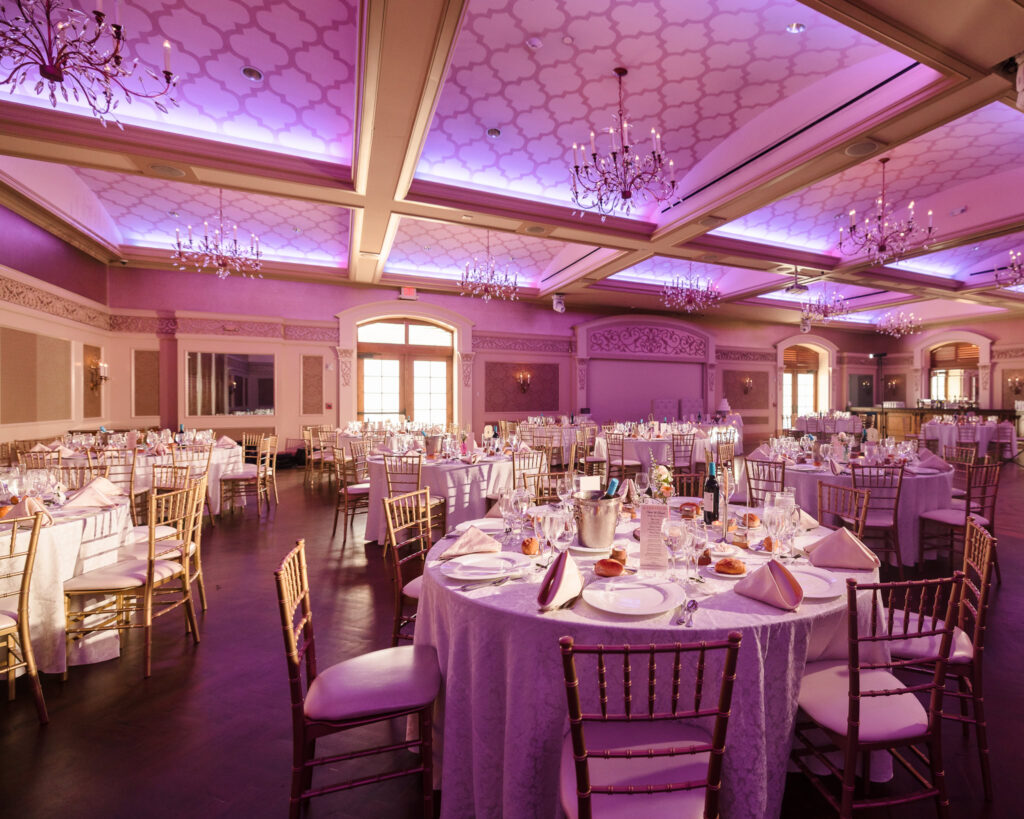 Elegant Larkfield Manor ballroom set for a wedding reception with gold chairs, round tables, and purple uplighting on Long Island.