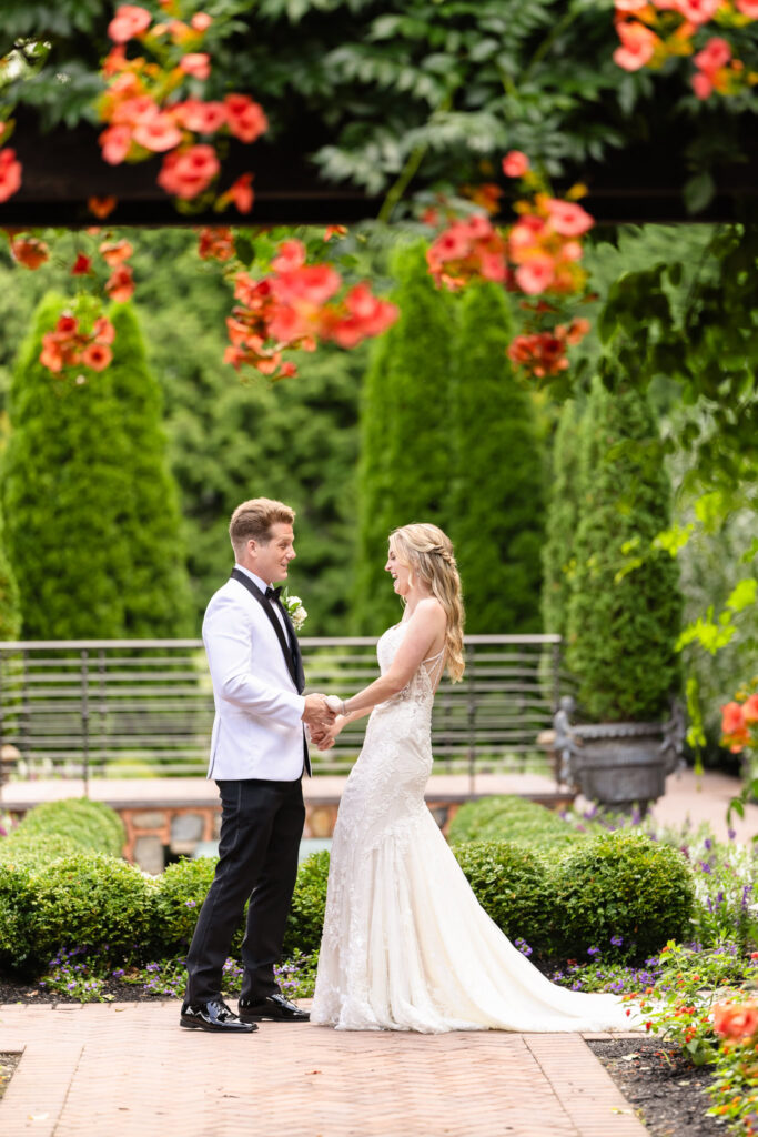 Bride and groom share a joyful first look in the garden courtyard at Larkfield Manor, surrounded by vibrant summer flowers and greenery.