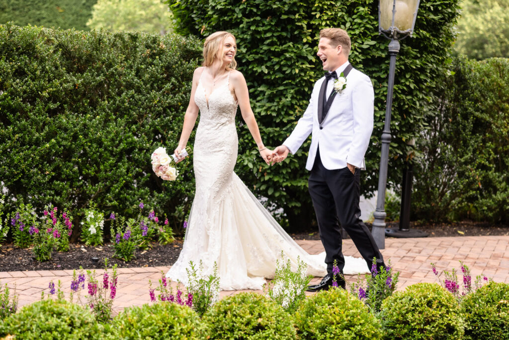 Bride and groom joyfully walking hand in hand through the lush garden pathways at Larkfield Manor on Long Island.
