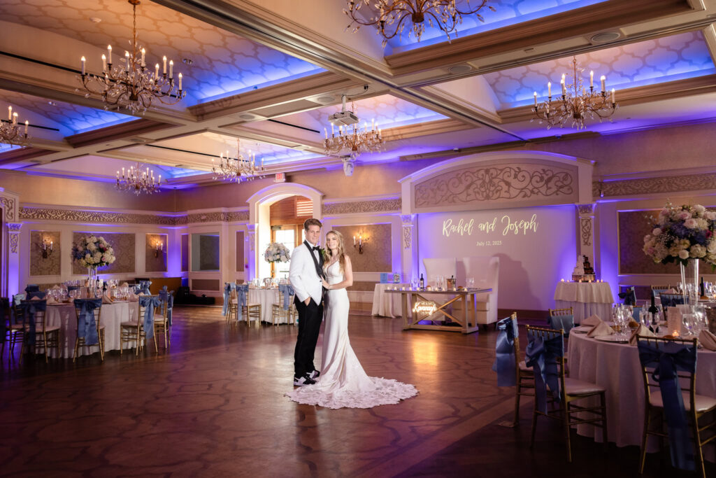 Bride and groom pose in the elegant ballroom at Larkfield Manor, surrounded by romantic blue uplighting and floral wedding décor on Long Island.