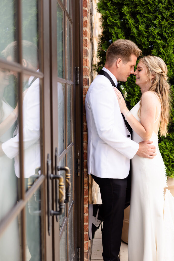 Bride and groom share an intimate moment by the brick wall and glass doors, reflecting elegant Long Island wedding romance.