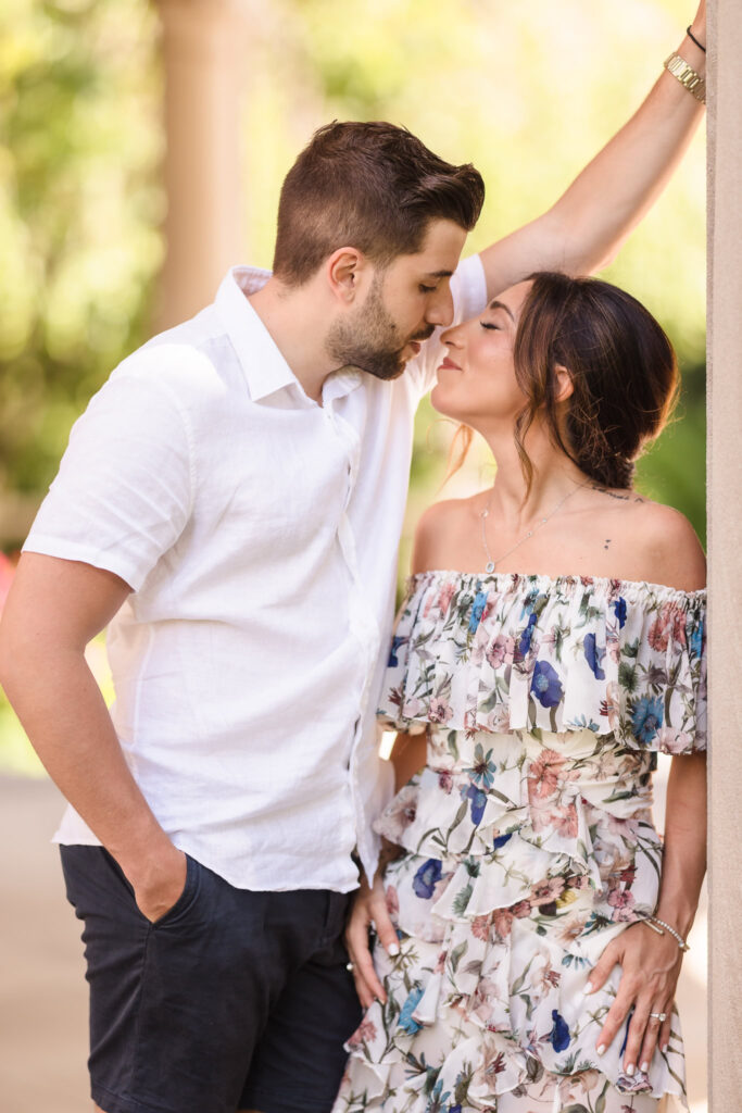 Romantic engagement photo of a couple sharing an intimate moment under the arches , with the woman in a floral off-shoulder dress and the man in a white shirt.