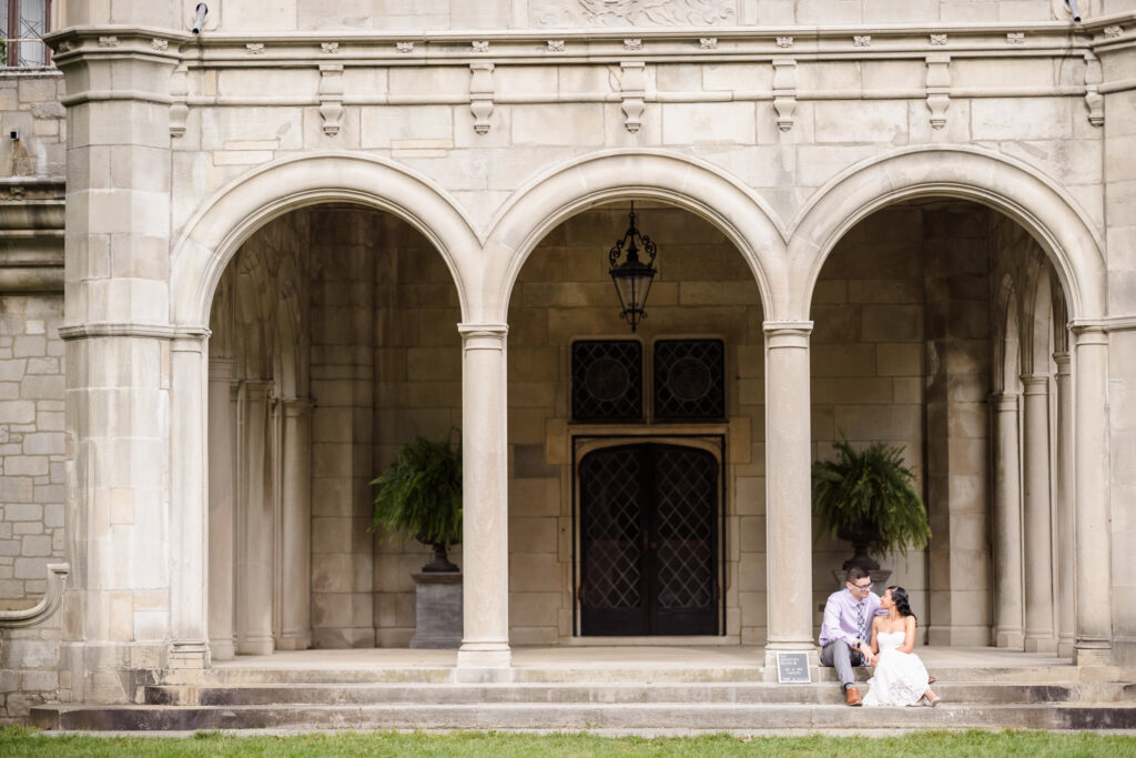 Elegant engagement photo of a couple sitting on the grand stone steps of Coe Hall Mansion at Planting Fields Arboretum in Oyster Bay, New York.