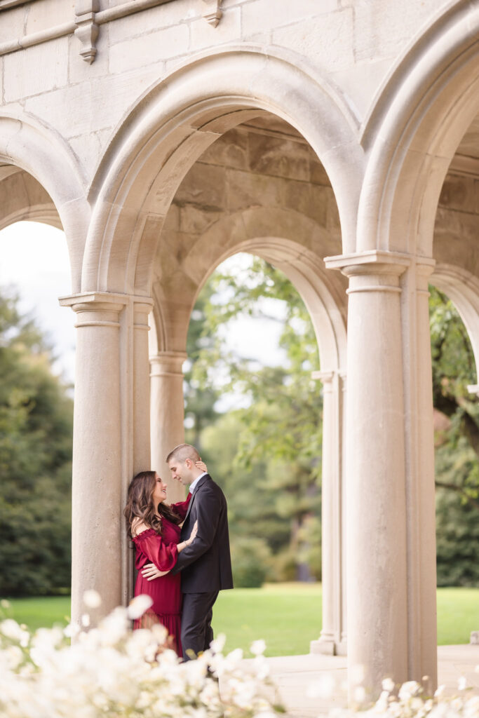 Elegant engagement photo of a couple embracing beneath the stone arches at Coe Hall in Planting Fields Arboretum, Long Island.