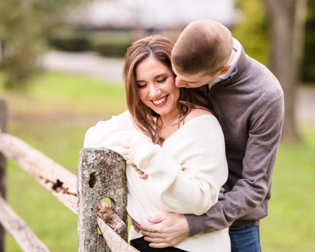 Tender engagement photo of a couple sharing a sweet moment by a rustic wooden fence