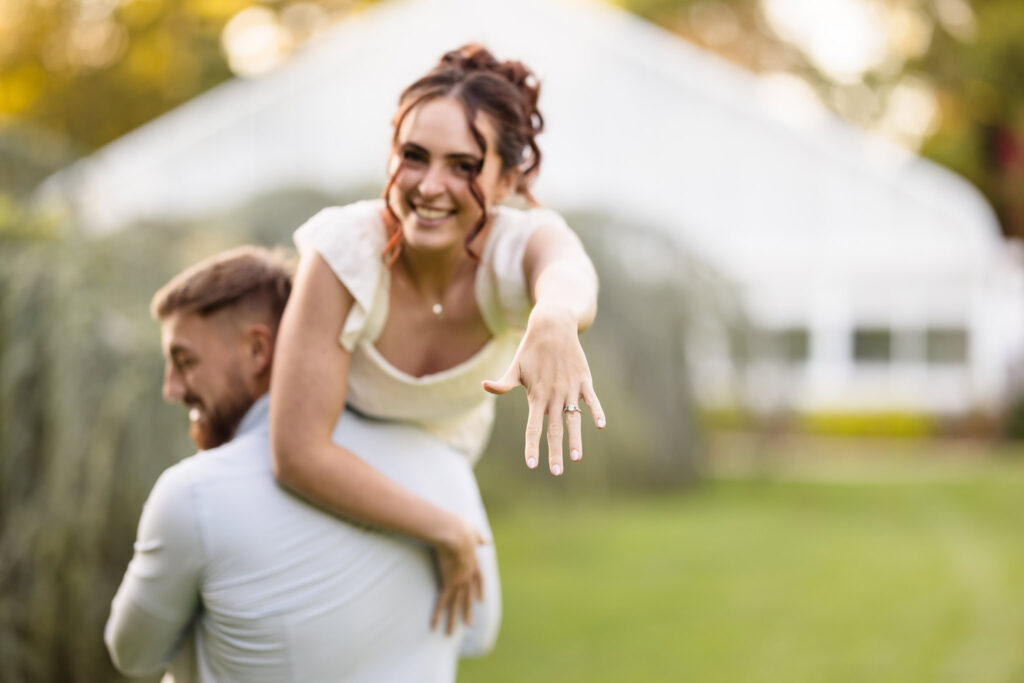 Playful engagement photo of a bride-to-be showing off her engagement ring while being carried by her fiancé 
