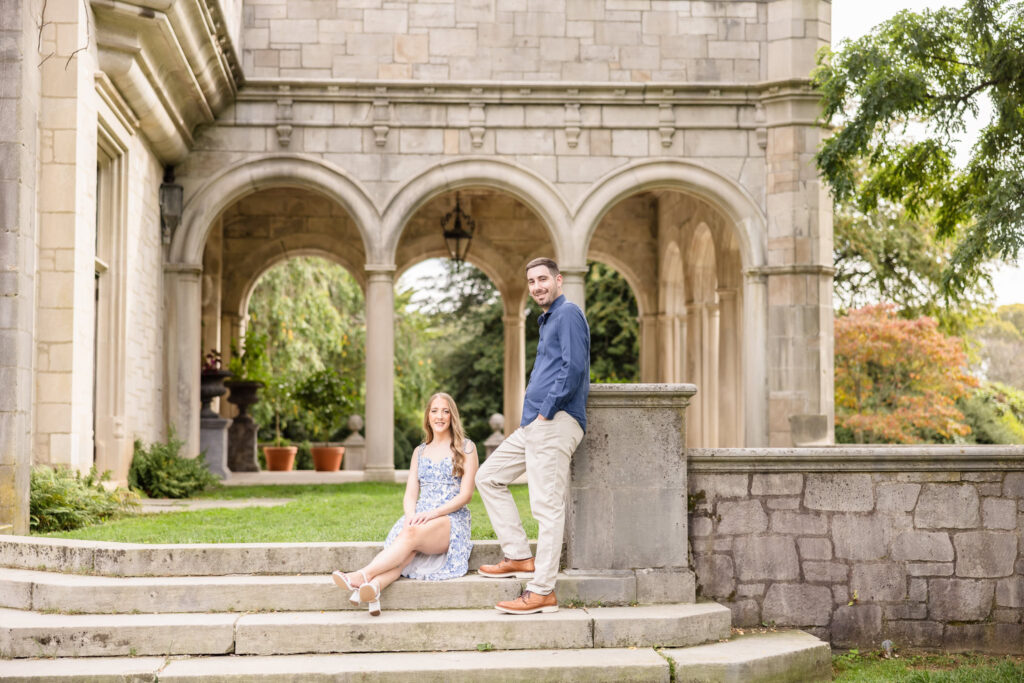 Elegant engagement photo of a couple posing on the stone steps of Coe Hall Mansion at Planting Fields Arboretum, featuring timeless architecture and lush greenery.