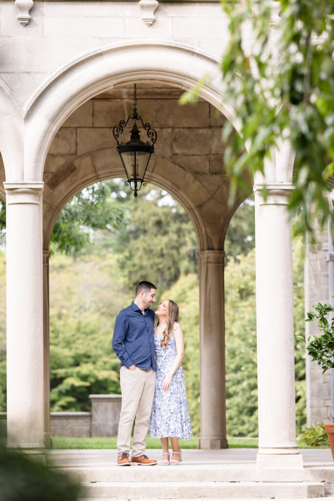 Couple standing beneath the elegant stone arches of Coe Hall during their fall engagement session at Planting Fields Arboretum in Oyster Bay, New York.