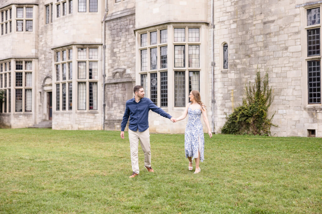 Couple walks hand in hand across the lawn of Coe Hall during their elegant fall engagement session at Planting Fields Arboretum in Oyster Bay, Long Island.