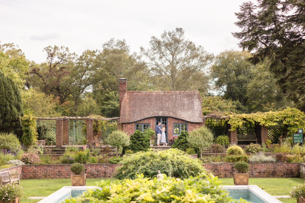 Couple shares a quiet moment in front of the charming brick cottage at the Italian Gardens during their fall engagement session at Planting Fields Arboretum in Oyster Bay, New York.