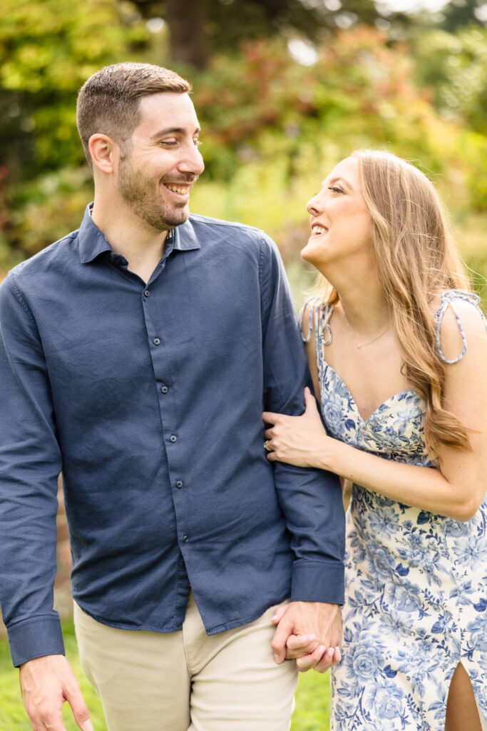 Couple laughs together while walking hand in hand during their joyful fall engagement session.
