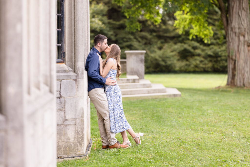 Couple shares a romantic kiss beside the stone architecture of Coe Hall during their fall engagement session at Planting Fields Arboretum in Oyster Bay, New York.
