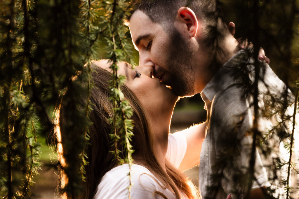 Romantic close-up of a couple kissing beneath hanging branches during their golden hour fall engagement session at Planting Fields Arboretum in Oyster Bay, New York.