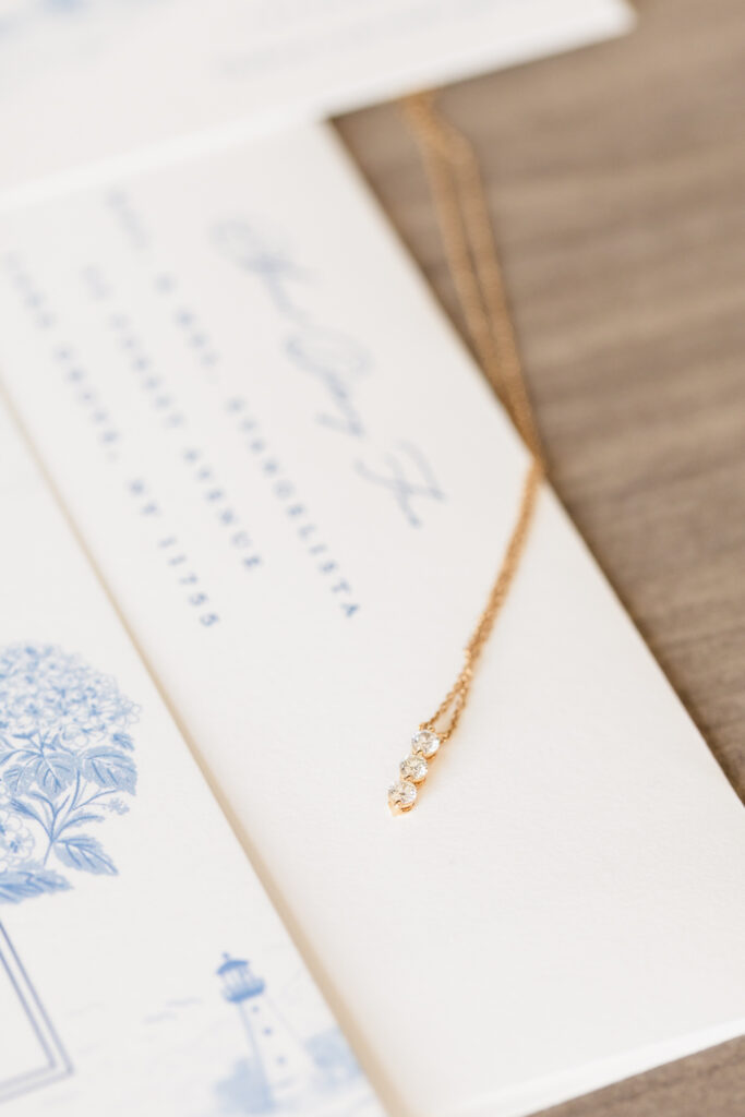 Delicate gold necklace with three diamonds displayed on coastal-themed wedding invitations for Andrea and Gillian’s Snapper Inn wedding in Oakdale, NY.