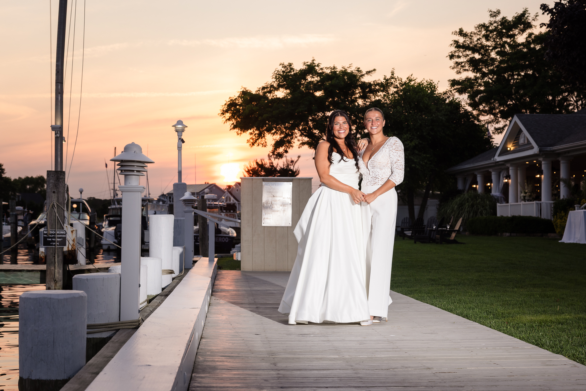 Brides posing on the dock at The Snapper Inn in Oakdale, Long Island, during sunset after their romantic waterfront wedding celebration.
