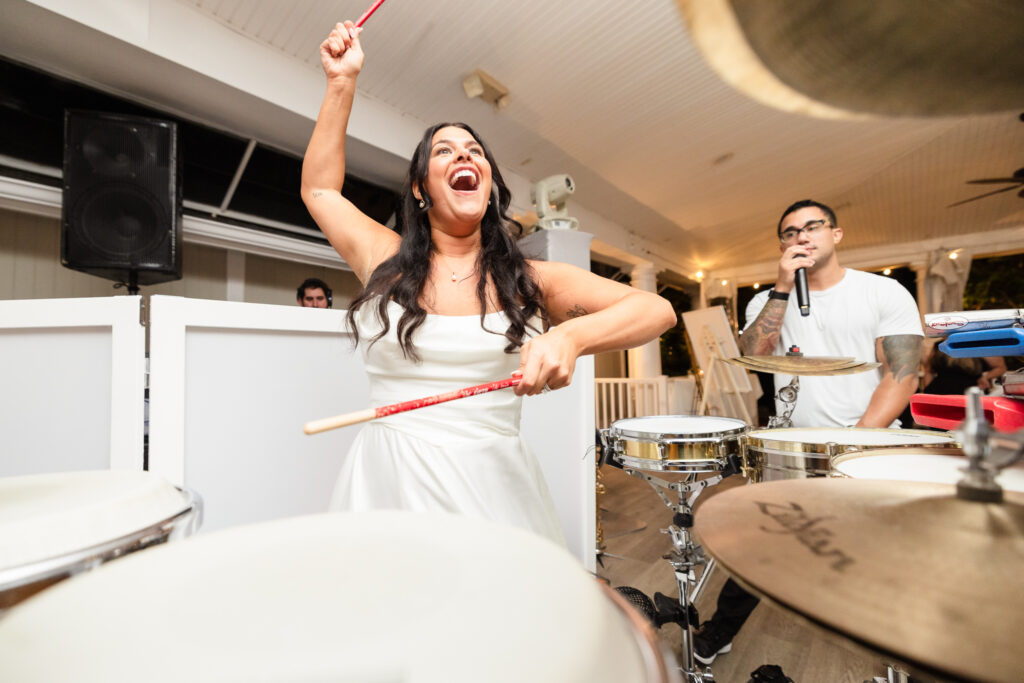 Bride playing the drums with excitement during the lively wedding reception at The Snapper Inn in Oakdale, Long Island.
