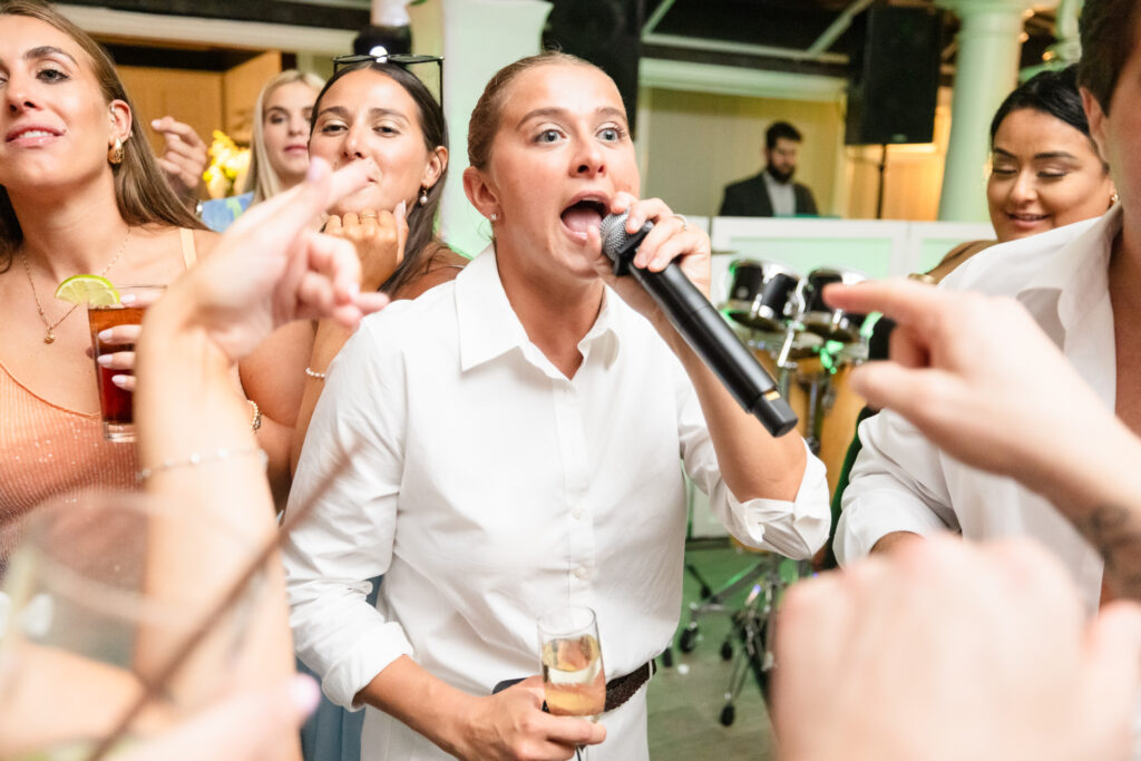 Bride singing into a microphone surrounded by friends during a lively wedding reception at The Snapper Inn in Oakdale, Long Island.