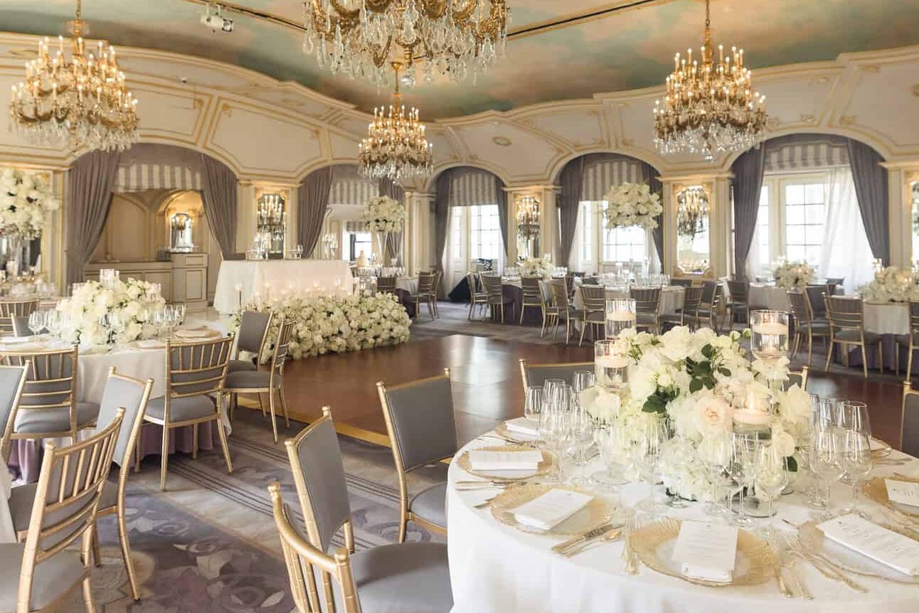 Wide view of the St. Regis New York wedding ballroom with painted sky ceiling, crystal chandeliers, and elegant white floral centerpieces.