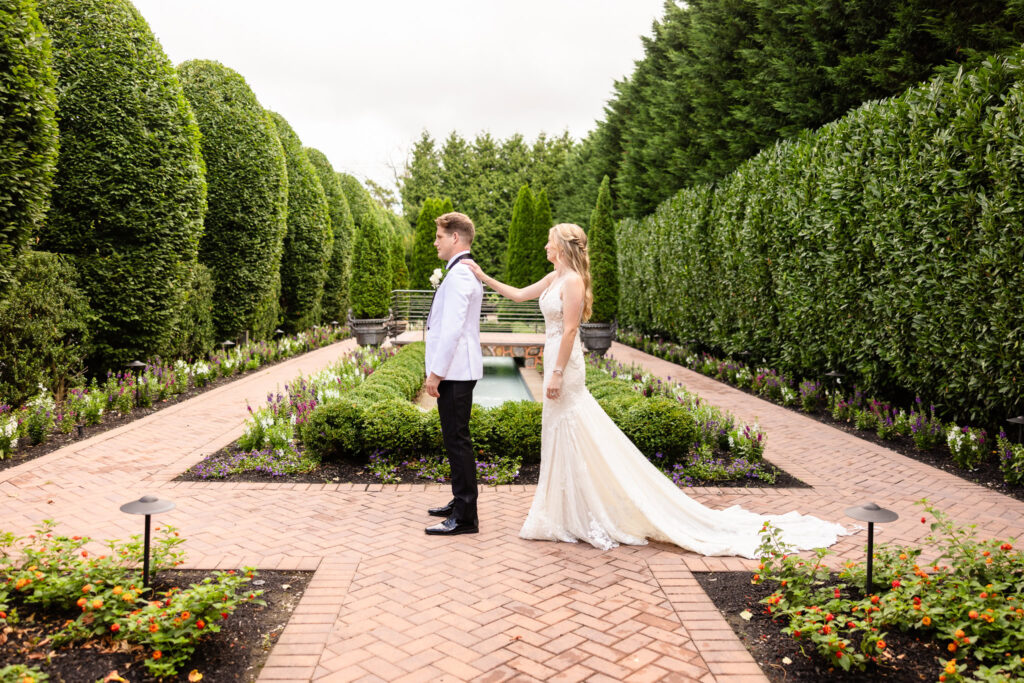 Bride touching groom’s shoulder during their emotional first look in the manicured garden at Larkfield Manor, captured by Heritage House Photography.