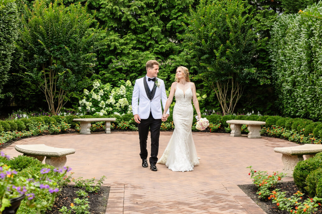 Bride and groom walk hand in hand through the lush garden courtyard at Larkfield Manor during their elegant summer wedding.