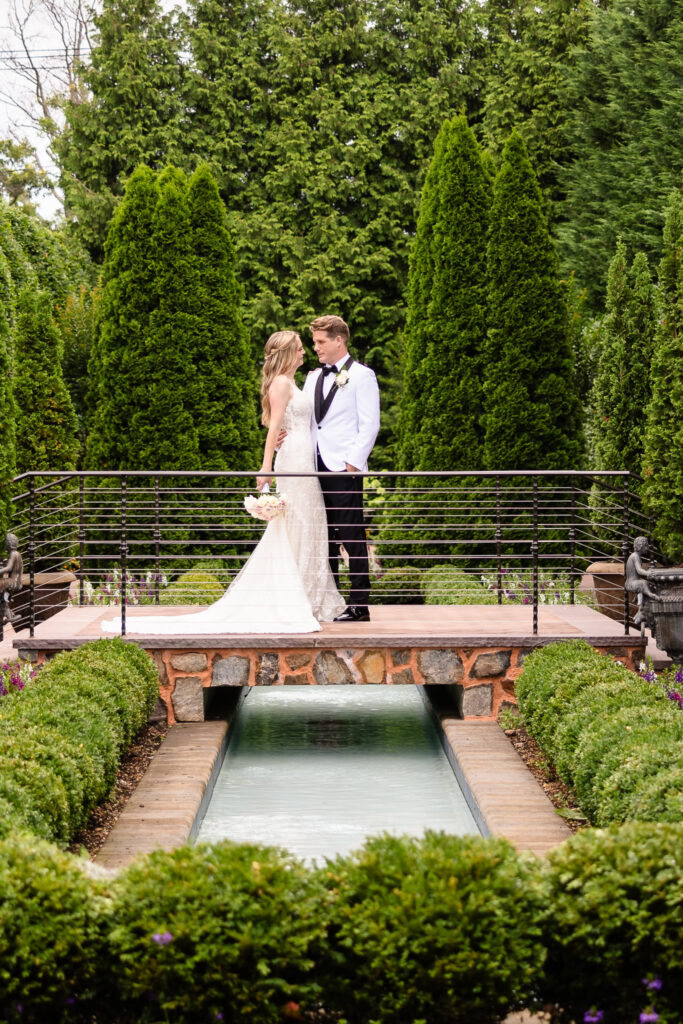 Bride and groom share a romantic moment on the garden bridge at Larkfield Manor surrounded by lush greenery.