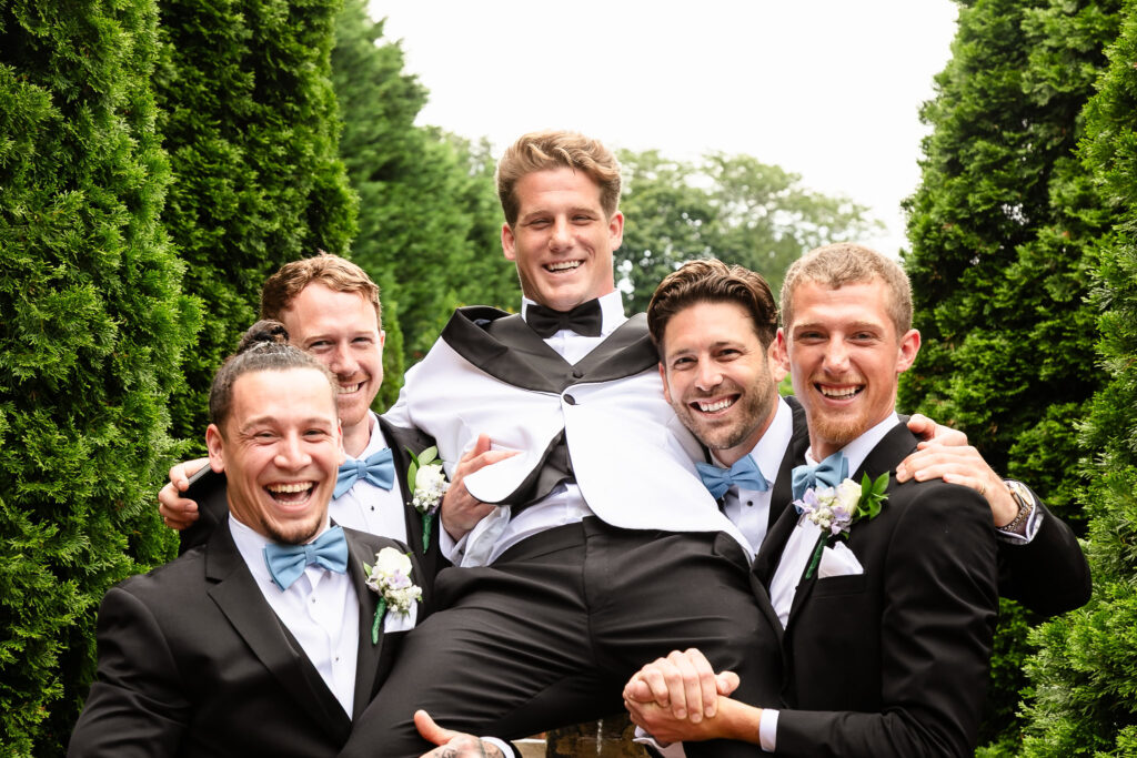 Groomsmen lift the groom in celebration, sharing laughter and joy during wedding portraits at Larkfield Manor.
