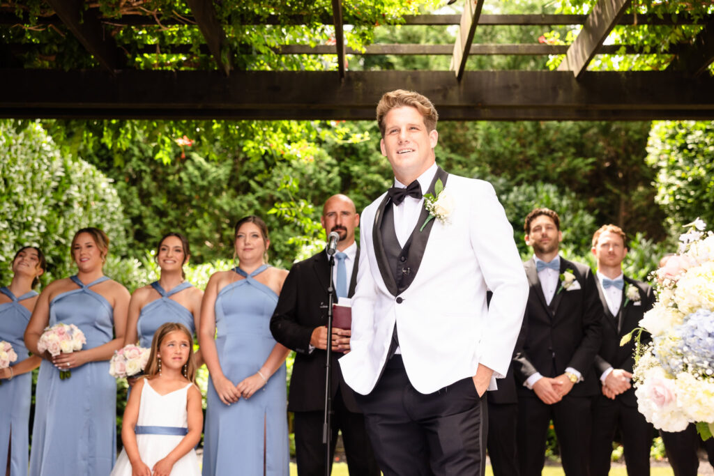 Groom waiting at the altar during an outdoor garden ceremony at Larkfield Manor, surrounded by bridesmaids in blue dresses and groomsmen in black tuxedos.