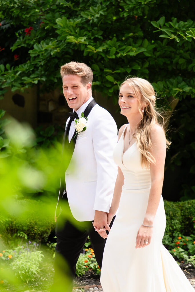 Bride and groom holding hands and smiling during their summer wedding at Larkfield Manor, surrounded by lush green gardens and natural light.