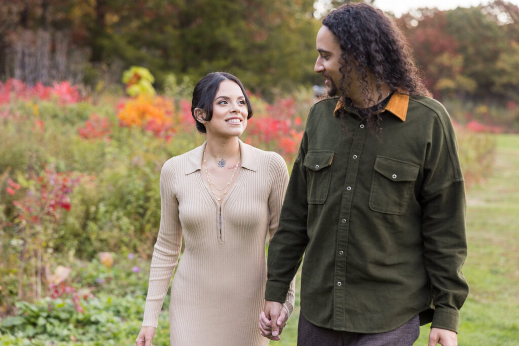 Couple walking hand in hand through vibrant fall foliage at Bethpage State Park during their autumn.