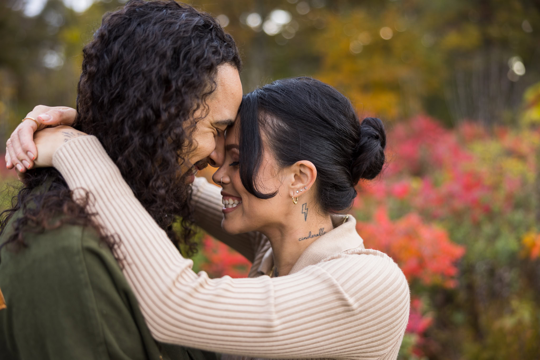 Couple laughing and touching foreheads, surrounded by colorful fall leaves during their engagement session at Bethpage State Park.